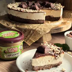 Ciasto Kinder Bueno bez pieczenia: kawałek na talerzu, obok słoik pasty orzechowej i orzechy.